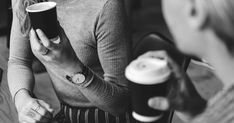 black and white photograph of two women holding coffee cups, one is looking at her phone