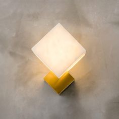 a square light sitting on top of a cement floor next to a white and yellow lamp