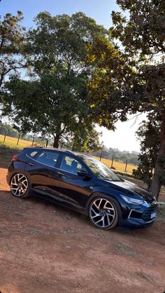 a blue car parked in front of some trees on a dirt road next to a field