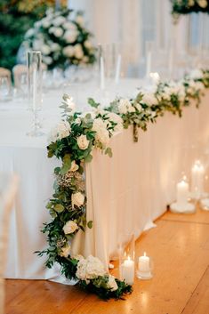 an arrangement of flowers and candles on a long table with white linen draped over it