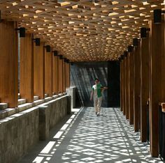 a person walking down a long walkway between two wooden structures with sun shining through them