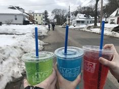 three people holding up two different colored drinks in their hands, with snow on the ground behind them