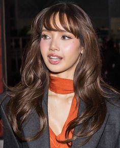 a woman with long hair wearing an orange shirt and black blazer is looking at the camera