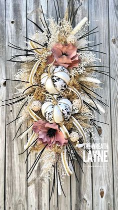 an easter wreath with feathers and eggs on it, hanging from a wooden fence in front of a weathered wood wall