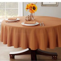 the table is set with an orange centerpiece and place settings on it, as well as sunflowers in a vase