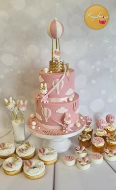 a pink and gold birthday cake surrounded by cupcakes