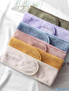 five towels folded on top of each other in different colors and sizes, sitting next to an open newspaper