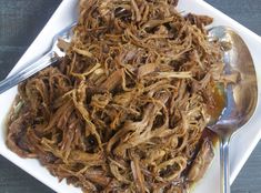 shredded beef on a white plate with a spoon and fork next to it, ready to be eaten