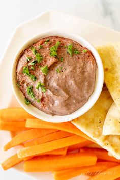 a white plate topped with carrots and guacamole next to tortilla chips