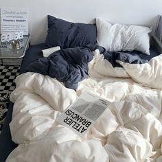 an unmade bed with blue and white sheets, pillows and a book on it