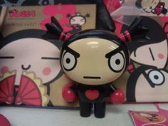 a small doll with black hair and red eyes sitting on a table next to other items