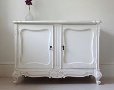 a white cabinet with two doors and a vase on top, against a plain wall