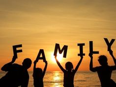 three people holding up letters that spell out the word family in front of an ocean at sunset