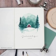 an open notebook with watercolor trees and a red house on the cover, surrounded by other office supplies