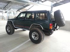 a green jeep with two large tires on it's flatbed in a parking garage