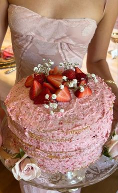 a woman holding a pink cake with strawberries on top and flowers in the middle