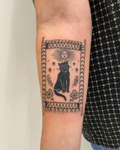 a black cat tattoo on the right forearm and arm with an ornate frame around it