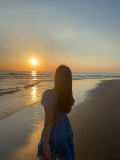 a girl walking on the beach at sunset with her back to the camera, looking out into the water