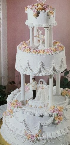 a three tiered wedding cake with roses on the top and groom standing next to it