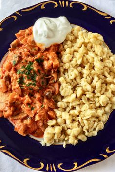 a blue plate topped with macaroni and cheese next to meat covered in sauce