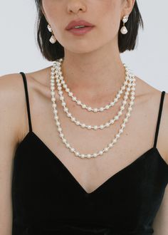 a woman in a black dress wearing two necklaces with pearls on the bottom and an earring