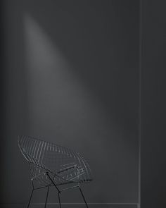 an empty chair in front of a gray wall with a light coming from behind it