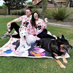 a man and woman are sitting on a blanket with two dogs in front of them