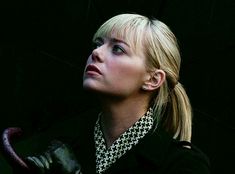 a woman with blond hair and black jacket holding an umbrella in her hand, looking up at the sky