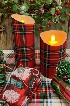 two red plaid candles sitting on top of a table next to christmas decorations and presents