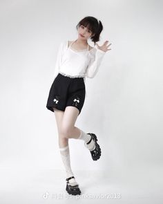 a woman in black shorts and white shirt posing for the camera with her hand up