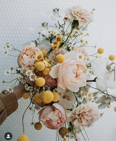 a person holding a bouquet of flowers with yellow and white blooms in it's center