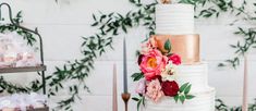 a three tiered white cake with pink and red flowers on top, surrounded by greenery