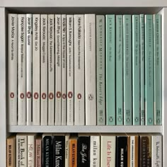 a book shelf filled with lots of books on top of each other in front of a white wall