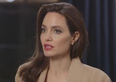 a woman with long brown hair wearing a tan jacket and earrings on her left shoulder