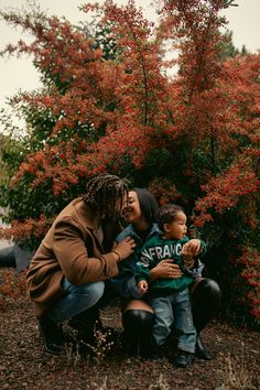 a woman kneeling down next to a little boy in front of some trees with red flowers