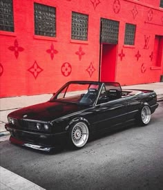 a black convertible car parked in front of a red building with graffiti on the wall