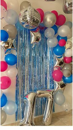 balloons and streamers are hanging from the ceiling in front of a wall with disco balls