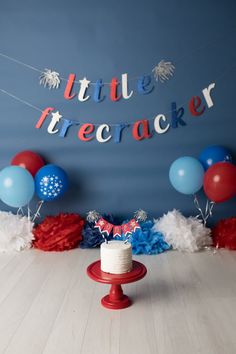 a cake on a red stand in front of balloons and streamers that say little firecracker