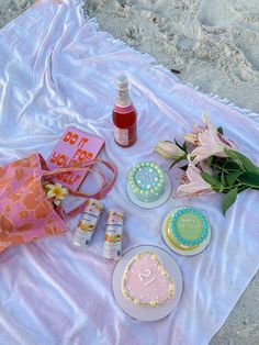 a table topped with cakes and flowers next to a bottle of boojute on top of a blanket