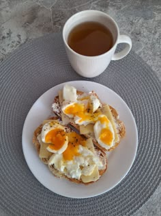 an egg and cheese sandwich on a plate next to a cup of tea or coffee