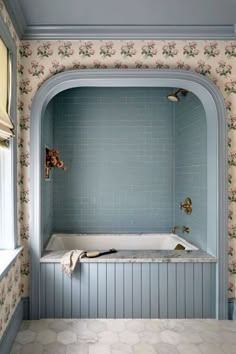 a bath tub sitting under a window next to a wall with flowers painted on it