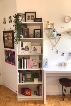 a white book shelf filled with books next to a desk and wall mounted pictures on the wall