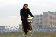 the man is riding his bike down the road in front of some buildings and water