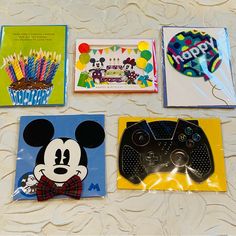 four birthday cards and a video game controller on a table with balloons, candles, and mickey mouse