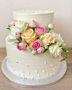 a three tiered white cake with pink and yellow flowers on it's side