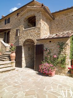 an old stone house with flowers in the front and stairs leading up to it's entrance