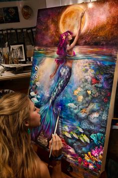 a woman is painting on an easel in front of a large canvas with a mermaid sitting on it