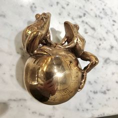 two brass frog figurines sitting on top of a ball