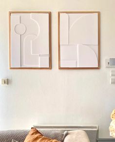 two framed art pieces hang on the wall above a couch in a white living room