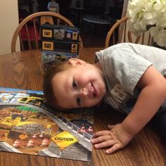 a young boy laying on top of a wooden table next to a puzzle board and flowers